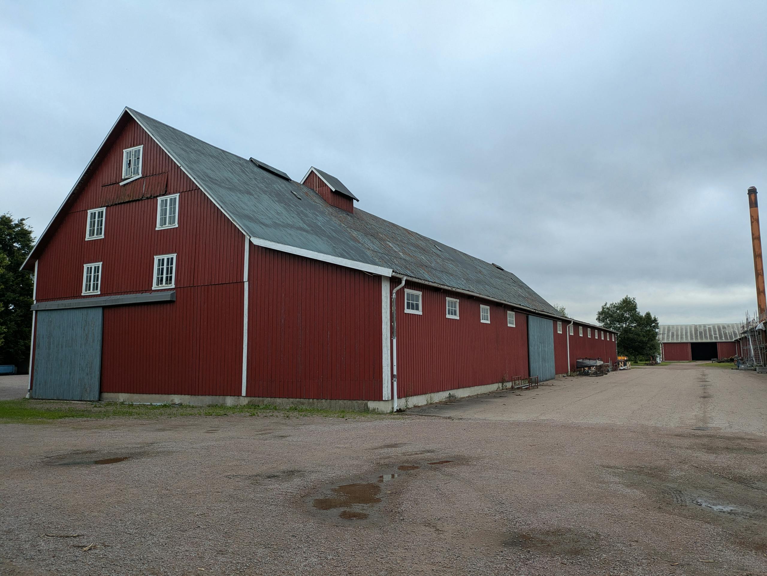 A large red barn with a metal roof in a rural setting under an overcast sky.